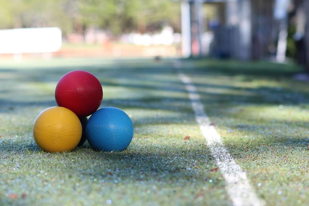 Three croquet balls in red, yellow and blue clustered on a club lawn beside a white line