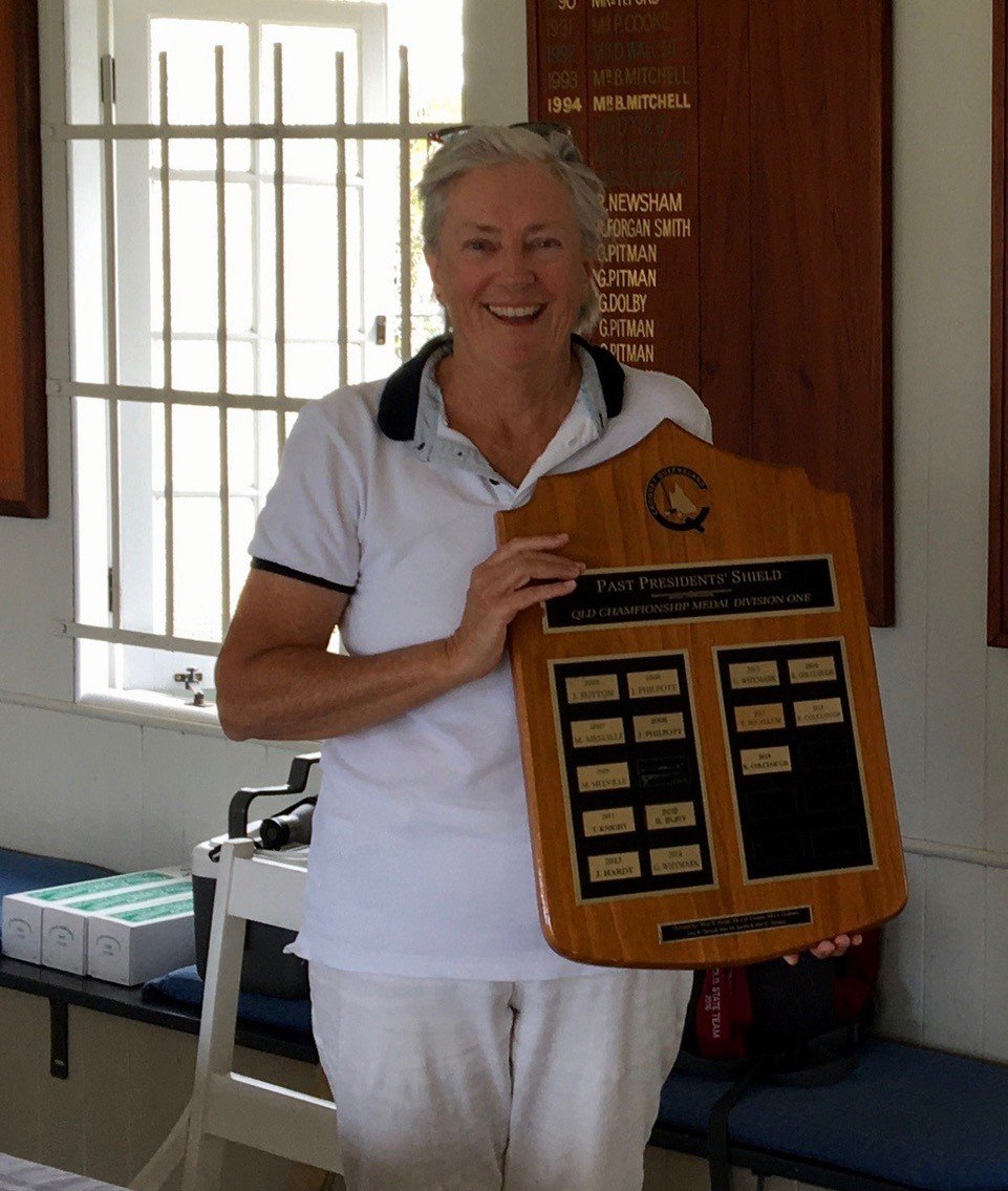 Woman holding Past Presidents Shield trophy inside club hall with honour board visible behind