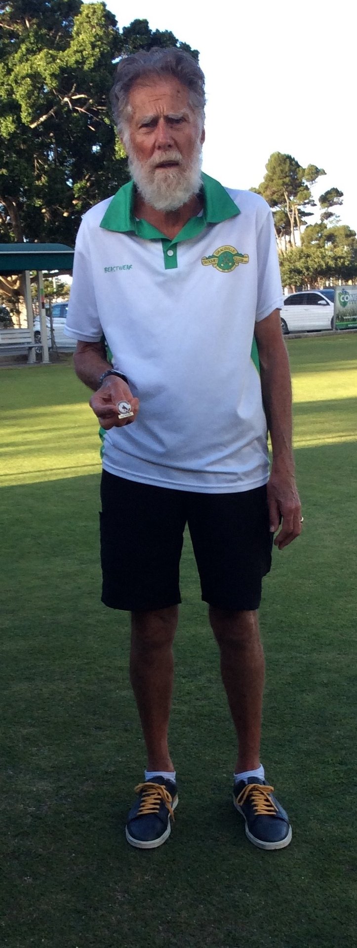 Man holding croquet ball on club lawn wearing white and green polo shirt
