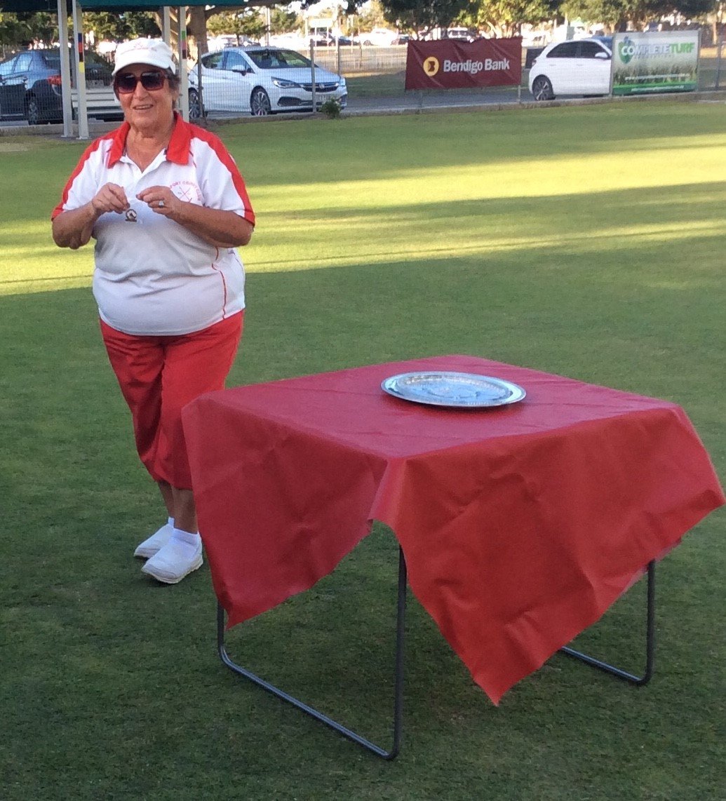 Woman in red and white attire standing beside table on croquet lawn during daytime event