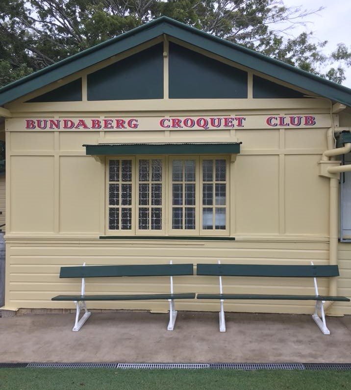 Bundaberg Croquet Club clubhouse with cream weatherboard exterior, benches on front lawn, surrounded by trees
