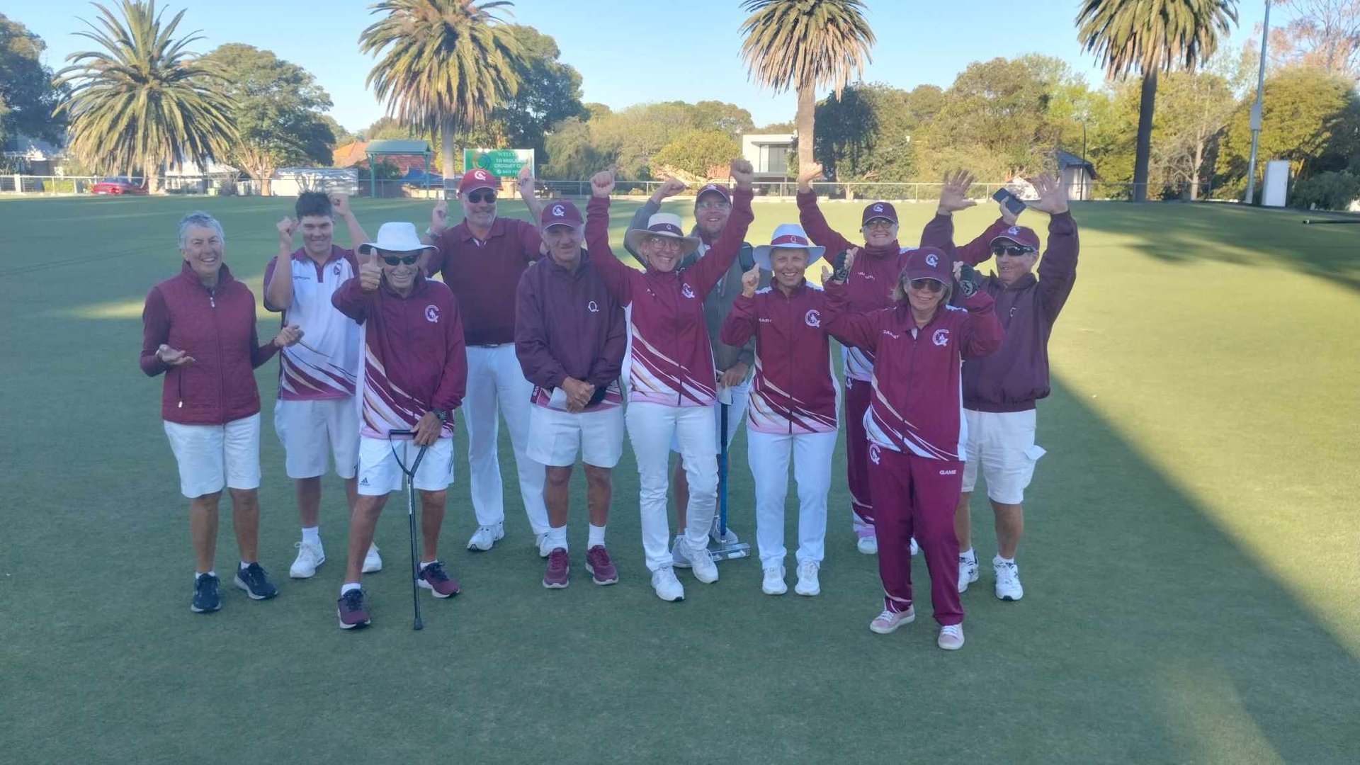 Team in maroon and white uniforms posing together on croquet lawn with palm trees and clubhouse visible