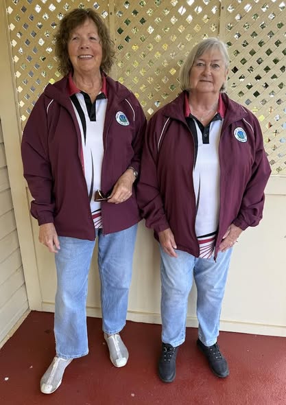 Two women stand side-by-side wearing matching maroon jackets with a croquet club logo and blue jeans