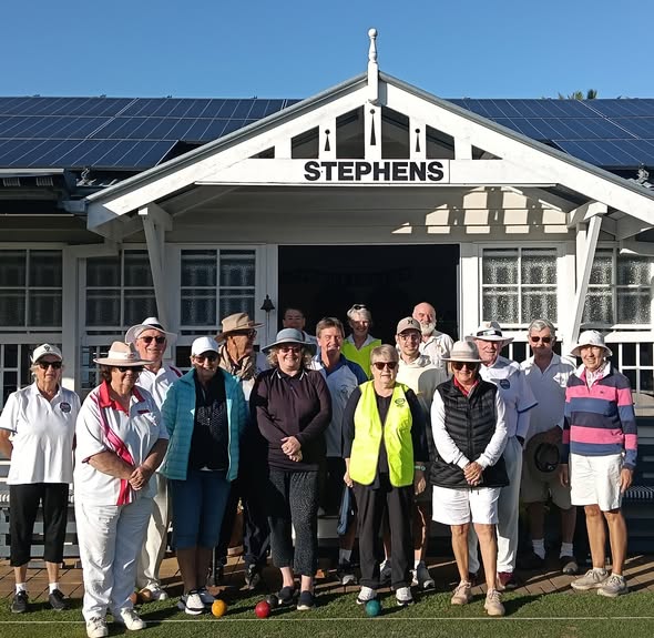 Croquet players pose with balls on the grass in front of the white Stephens clubhouse with solar panels
