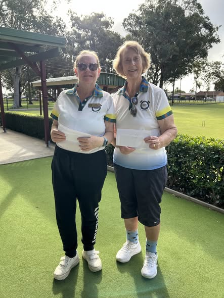Two women in croquet uniforms stand on a green lawn, holding certificates at a croquet event