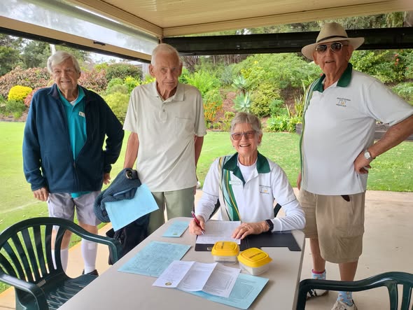 Four people at a croquet club pavilion, with one woman signing documents at a table while others observe