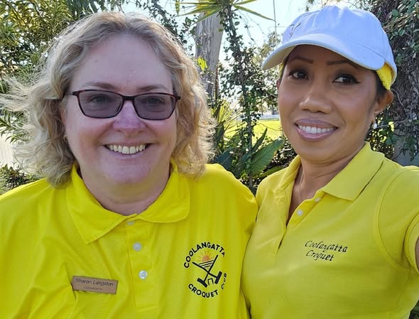 Two women in yellow Coolangatta Croquet Club polo shirts and caps smile for a selfie outdoors