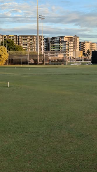 A croquet lawn with wickets and a mallet, set against a backdrop of apartment buildings and stadium lights