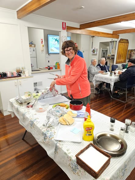 A woman in a pink jacket prepares food at a table with croquet equipment visible in the background