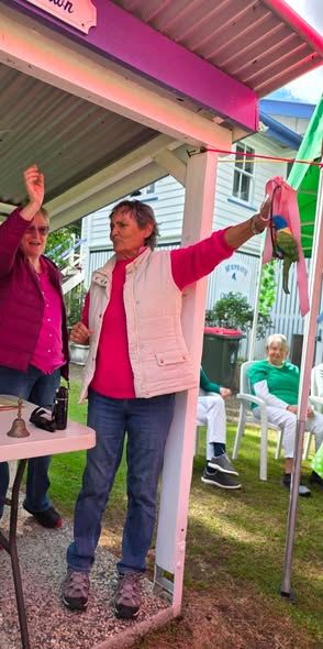A woman in a pink vest raises her arm to hit a croquet ball with a mallet under a pink canopy at a croquet event
