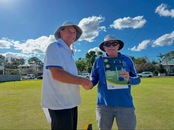 Two men shake hands on a croquet lawn; one holds a "Golf Summer" booklet, indicating a croquet event under a sunny sky
