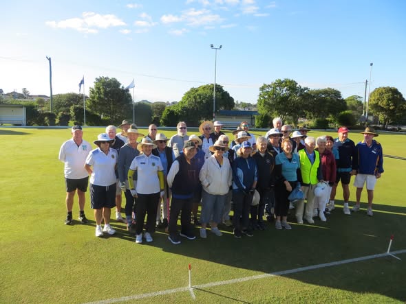 A group of croquet players poses for a photo on a sunny lawn, with mallets and wickets visible, indicating a club event or tournament