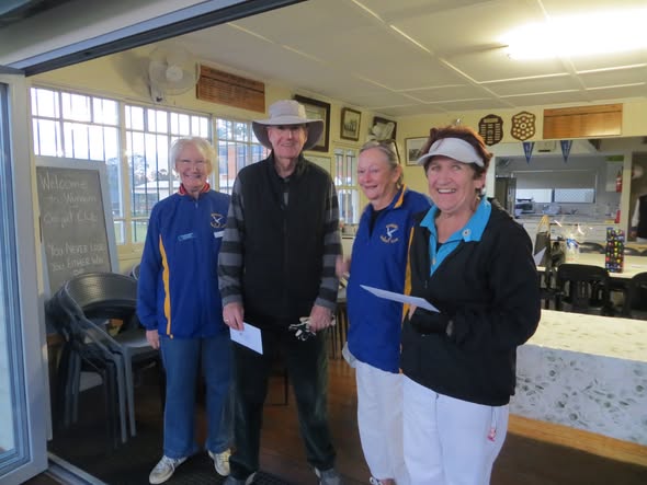 Four people in croquet club attire stand inside a clubhouse, holding papers, with a "Welcome to Warrnambool Croquet Club" sign visible
