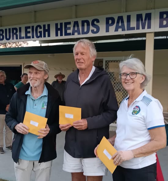 Three people stand in front of the Burleigh Heads Palm B Croquet Club, holding yellow envelopes, likely award certificates