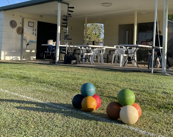 Colorful croquet balls arranged on a grass lawn near a club house with tables and chairs