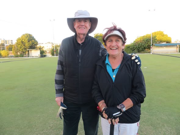 Two people pose together on a croquet lawn, one holding a mallet, with croquet hoops visible in the background