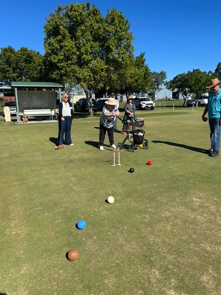 Players enjoy a game of croquet on a sunny day, with balls and wickets on the lawn
