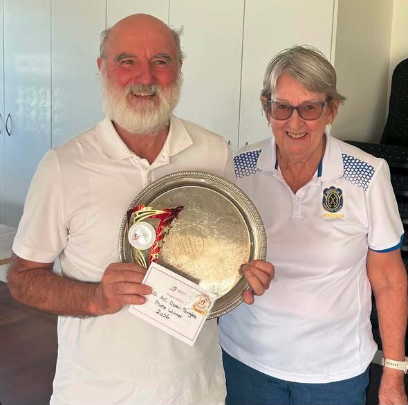 A man and woman in croquet attire hold a silver trophy and certificate for the 2024 AC Open Singles Plate Winner