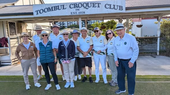 Group of croquet players posing in front of Toombul Croquet Club sign, established 1928, on a sunny day