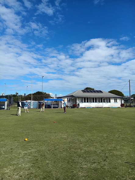 Players on a croquet lawn under a blue sky, with a clubhouse and solar panels in the background