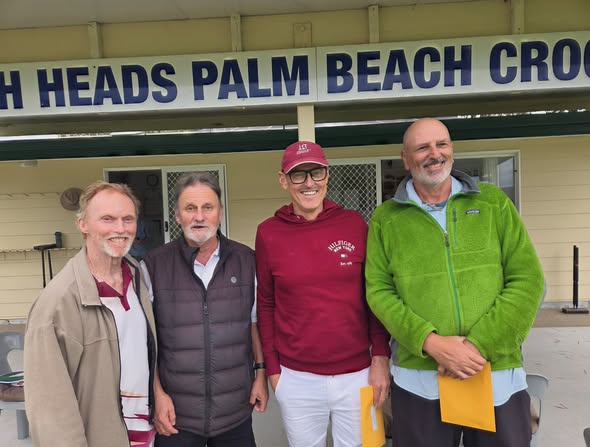 Four people stand smiling in front of the "Palm Beach Croquet" club sign, with one holding a yellow scorecard, indicating a croquet event