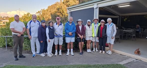 A group of croquet players in casual attire pose for a photo outside a club pavilion, with one holding a croquet mallet