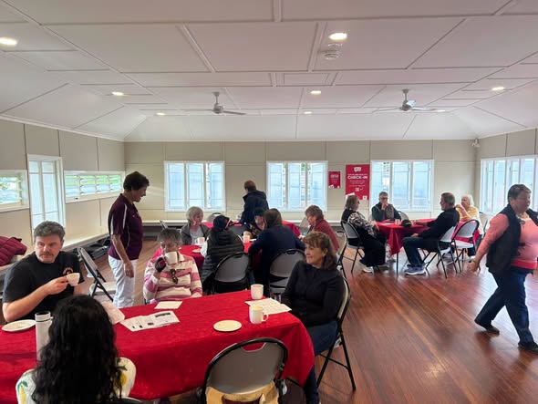 People gather at red-clothed tables inside a croquet club hall, drinking tea and socializing during a casual event
