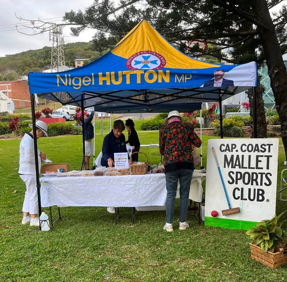 People at a croquet event under a "Nigel Hutton MP" tent, with a "Cap. Coast Mallet Sports Club" sign and croquet equipment visible